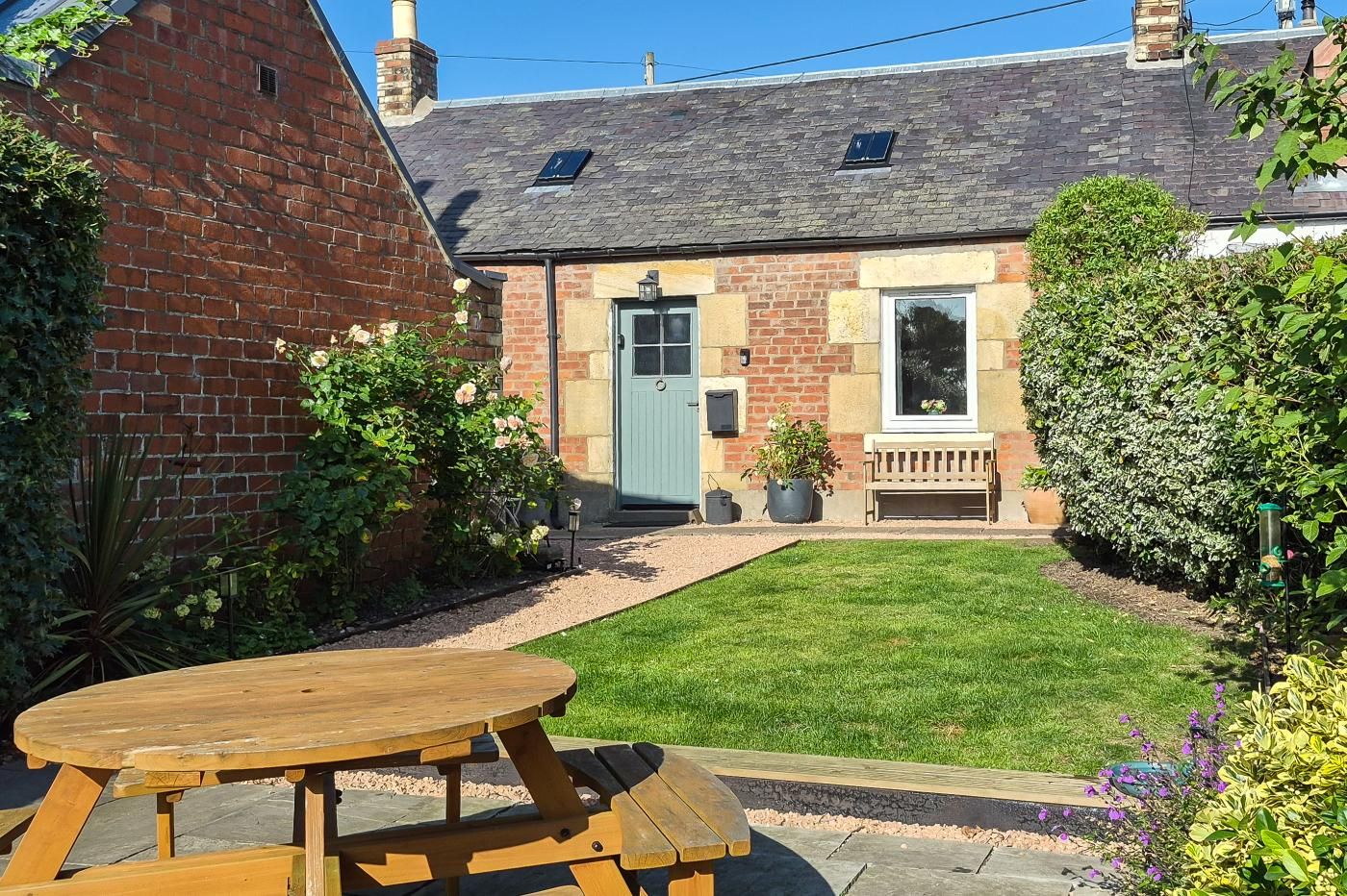 A brick house with a front door, a small porch, and a garden with a lawn and potted plants.