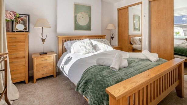 A neatly arranged bedroom with a wooden bed, two bedside tables, a mirror, and a wardrobe.