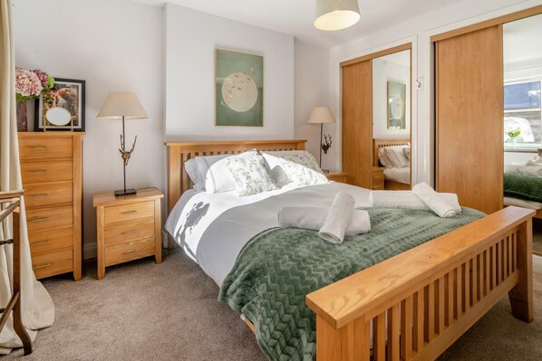 A neatly arranged bedroom with a wooden bed, two bedside tables, a mirror, and a wardrobe.