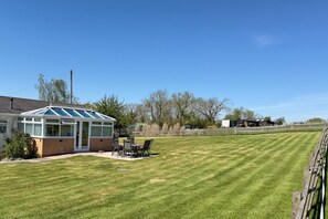 A house with a conservatory, a lawn, and a fenced area.