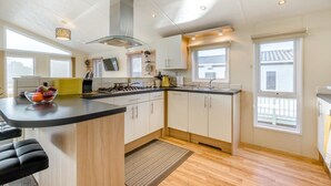 A modern kitchen with a central island, a built-in stove, and a large window. - 3 Bed in Burgh Castle, Great Yarmouth (oc-f34452) (Burgh Castle)