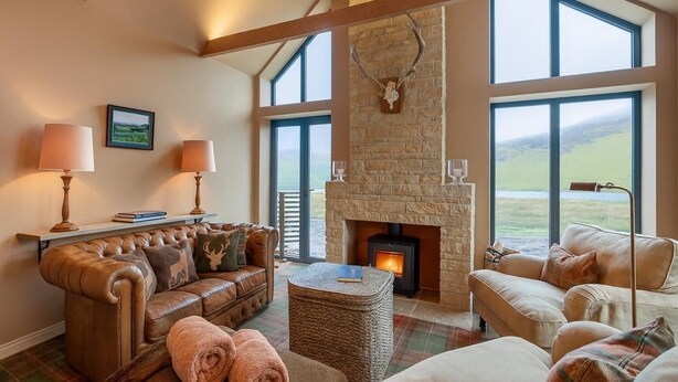 Amplia sala de estar con chimenea de piedra, sofás de cuero y grandes ventanales con vistas al exterior.