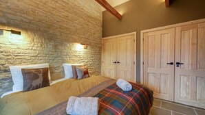 Un dormitorio con pared de piedra, una cama con manta escocesa y armarios de madera.