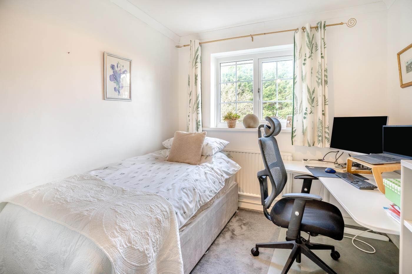 A bedroom with a single bed, a desk with a computer, and a window with curtains.