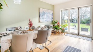 Zona pranzo con tavolo apparecchiato per quattro persone, divano e ampia finestra con vista sul giardino.