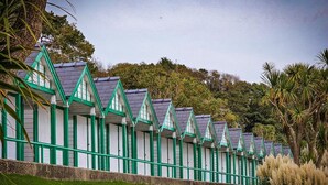 Una serie di edifici uniformi con tetti verdi, pareti bianche e decorazioni verde, allineati lungo una zona erbosa con alberi sullo sfondo.