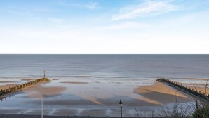 A coastal scene with a clear sky, calm sea, and a wooden jetty extending into the water. - 2 Bed in Sheringham (oc-b34382) (Sheringham)