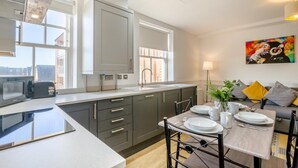 A modern kitchen with grey cabinets, a large island, and a dining area with a table set for four. - 2 Bed in Sheringham (oc-b34382) (Sheringham)