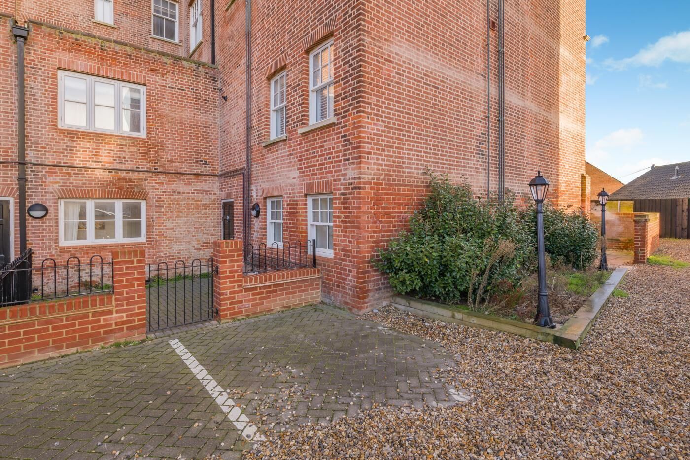 A red brick building with multiple windows, a gated entrance, and a gravel driveway.