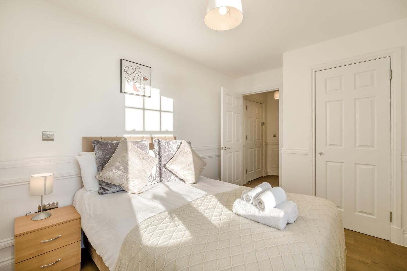 A neatly arranged bedroom with a bed, bedside lamp, and a framed picture on the wall.