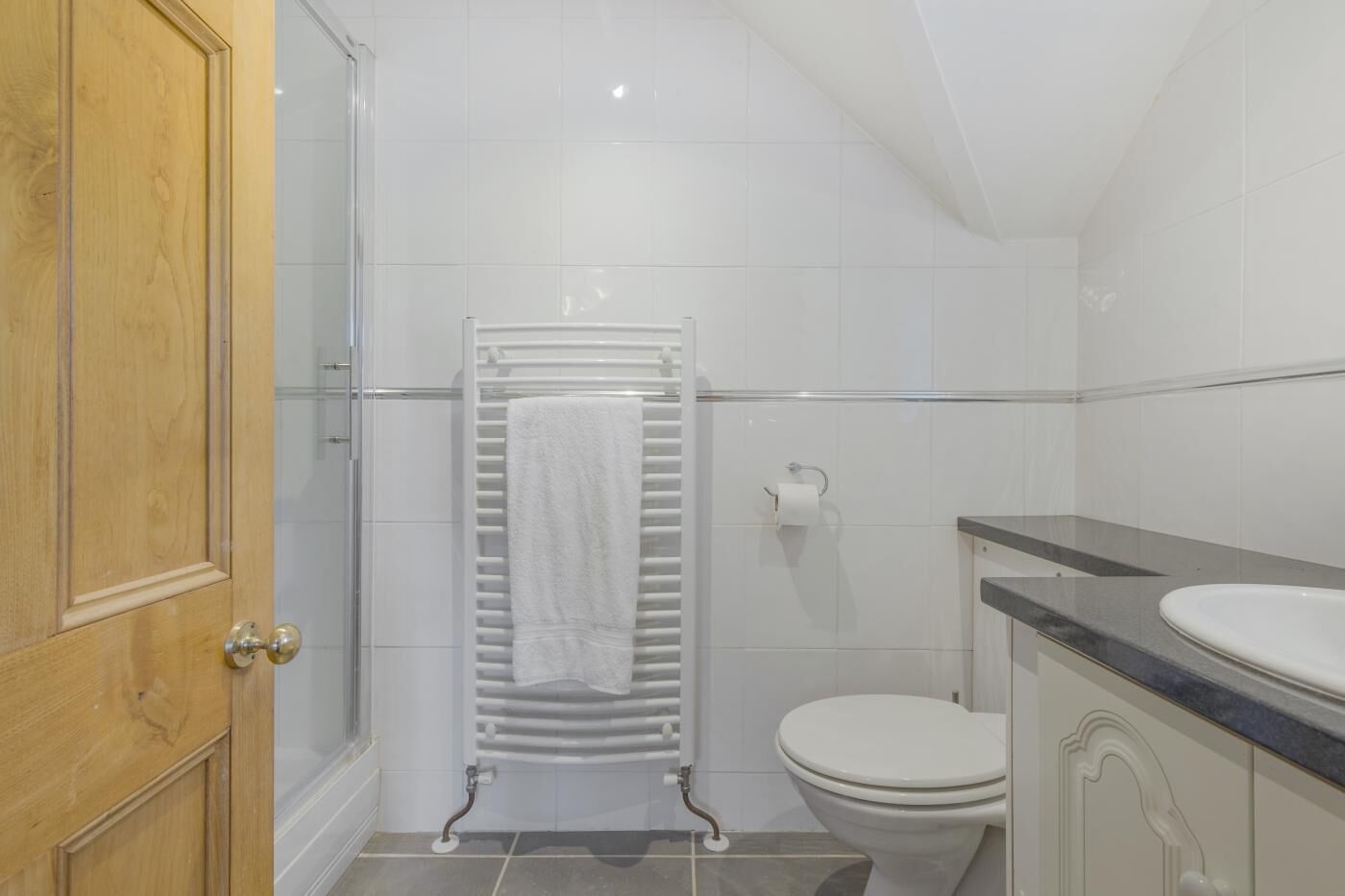 A bathroom with a wooden door, a glass shower enclosure, a white towel on a towel rack, a toilet, and a sink with a countertop.