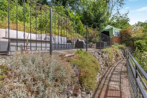A pathway leading to a green tent-like structure, surrounded by a metal fence and various plants. - 7 Bed in Matlock Bath (oc-n34368) (Matlock Bath)