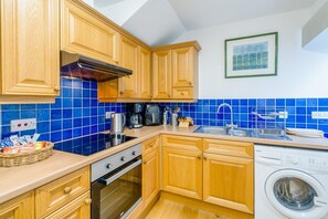 Une cuisine avec des meubles en bois, un four encastré, un lave-linge et un crédence en carreaux bleus.
