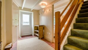 Un couloir avec un escalier en bois, une porte et une petite table.