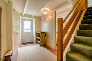 A hallway with a wooden staircase, a door, and a small table. - 3 Bed in St. Merryn (oc-l34453) (Porthcothan Bay)