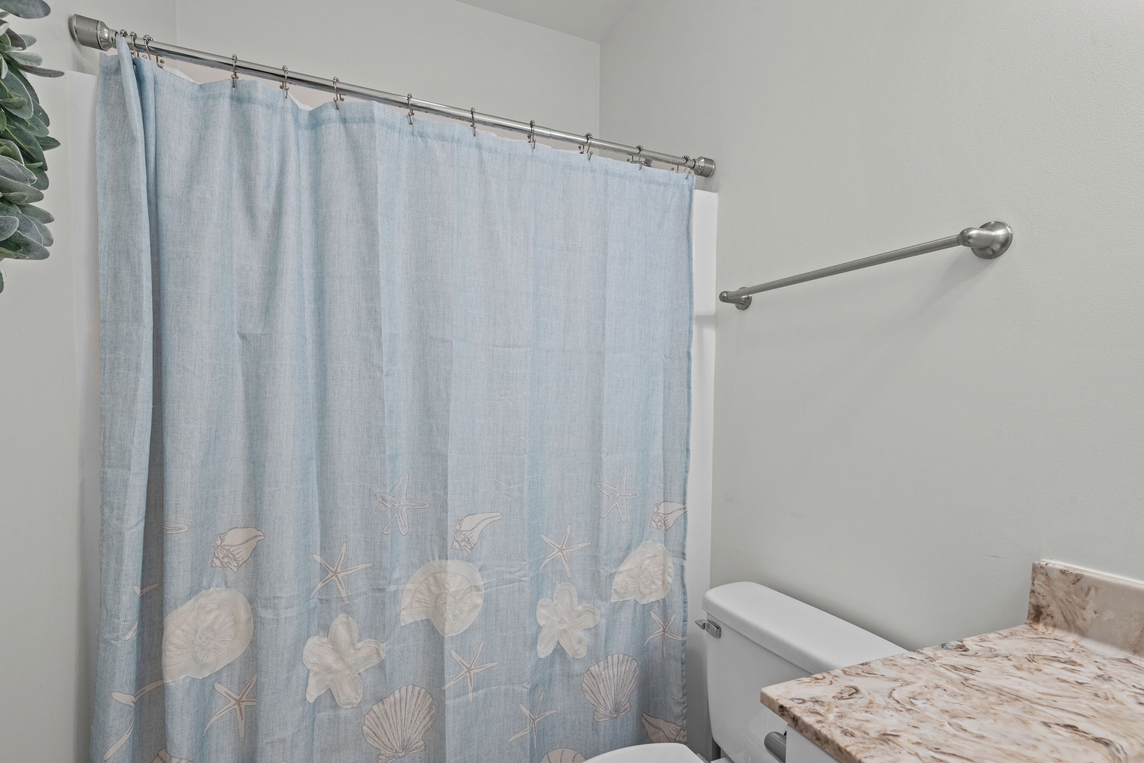 A bathroom with a light blue shower curtain featuring a sea shell and starfish pattern, a white toilet, and a marble sink.