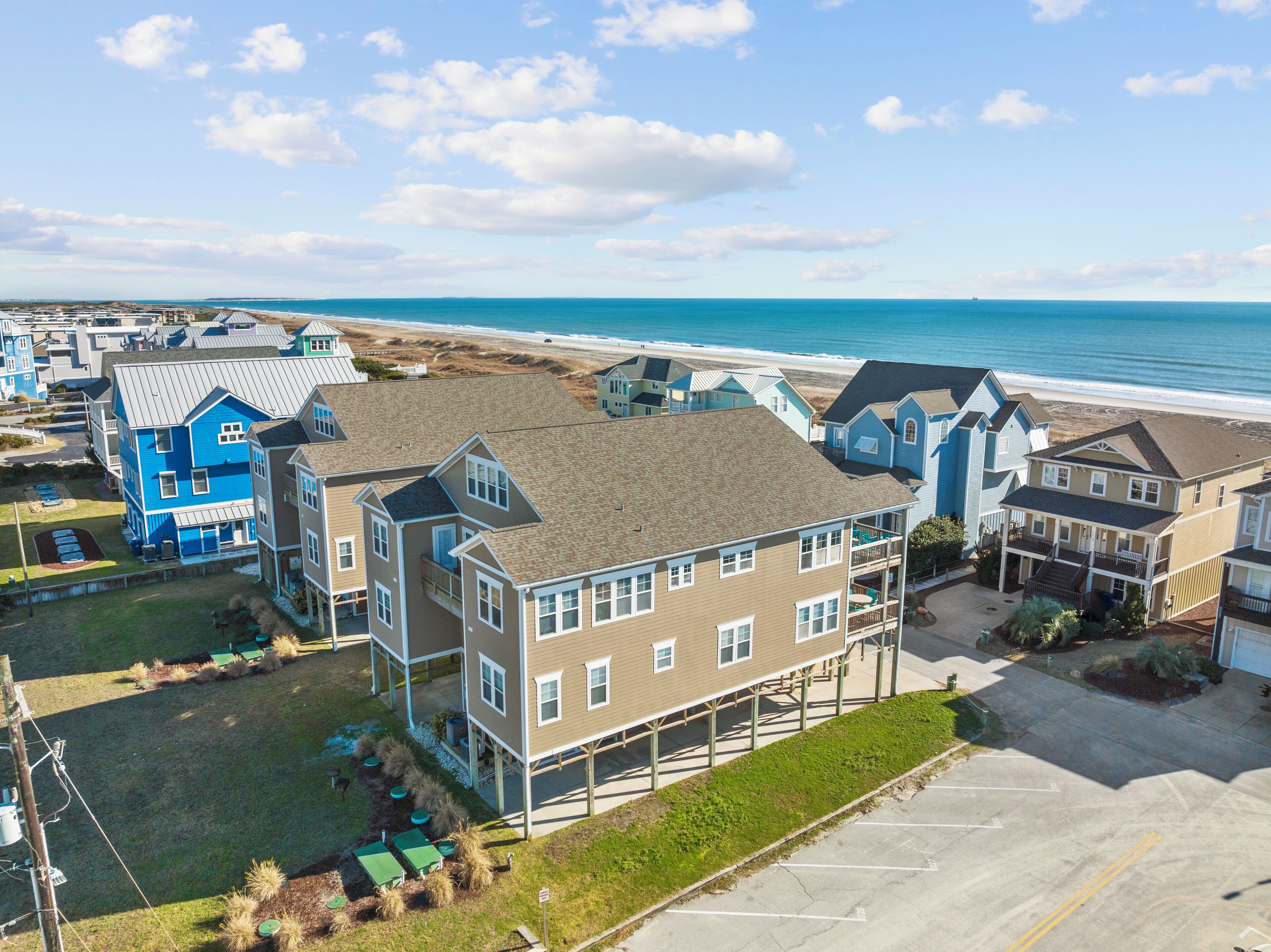 A coastal residential area with multiple two-story houses, a parking lot, and a beach in the background.