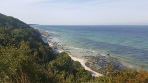 Paesaggio costiero con spiaggia, costa rocciosa e vegetazione lussureggiante.