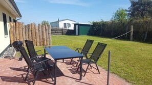 Patio esterno con tavolo e sedie, barbecue e recinzione.