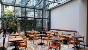A cafe with tables and chairs arranged in a spacious, well-lit room with large windows and a patterned floor. - Molokan Inn Hotel (Baku)