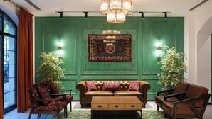 A room with a green wall, a patterned rug, a sofa, two armchairs, a coffee table, and a chandelier. - Molokan Inn Hotel (Baku)