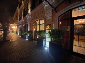 Um hotel com fachada clássica, grandes janelas e plantas em vasos na entrada.