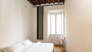 A bedroom with a bed, a window, a radiator, and a wooden floor. - Vicolo Santa Rufina Apartment - Trastevere (Roma)