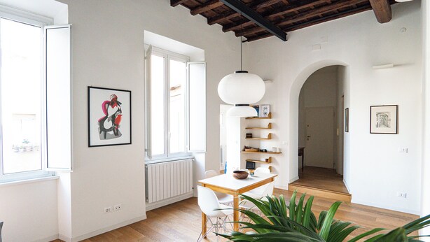 A spacious living area with a wooden floor, a dining table with chairs, a large plant, and a white pendant light. - Vicolo Santa Rufina Apartment - Trastevere (Roma)