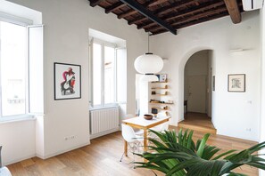 Amplia sala de estar con piso de madera, una mesa de comedor con sillas, una planta grande y una lámpara colgante blanca.