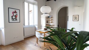 A dining area with a wooden table and chairs, a white pendant light, and a potted plant. - Vicolo Santa Rufina Apartment - Trastevere (Roma)