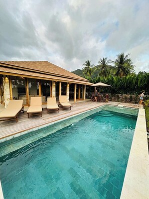 A pool area with lounge chairs and a covered seating area. - Villa Lily Bay (Selong Belanak)
