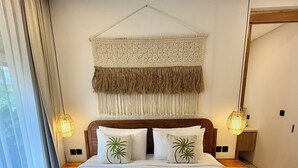 Een netjes opgemaakt bed met twee kussens, een geweven hoofdbord en een hangend macramé kunstwerk erboven.