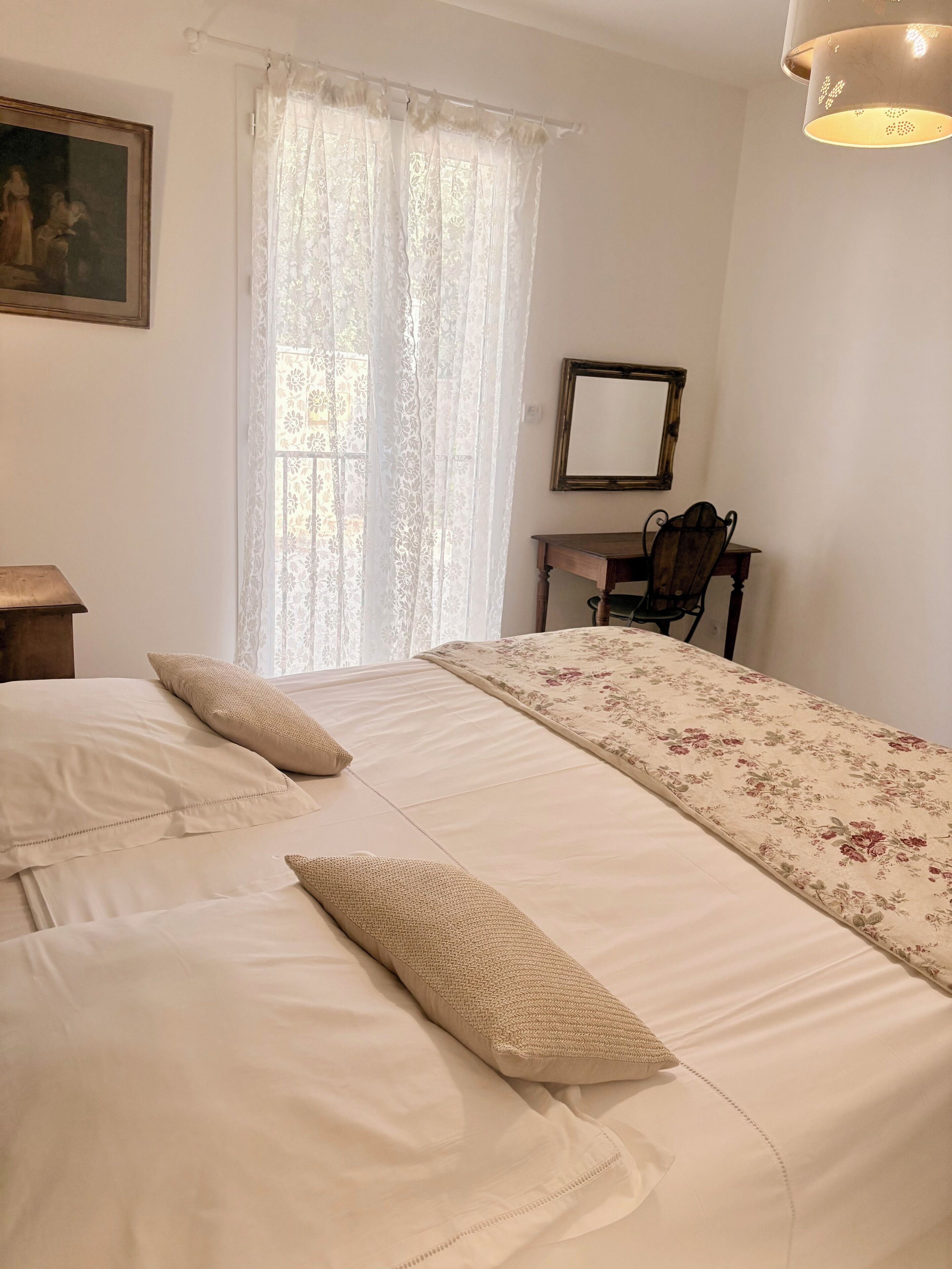 Un dormitorio con dos camas, un escritorio, una silla, un espejo y una ventana con cortinas de encaje.