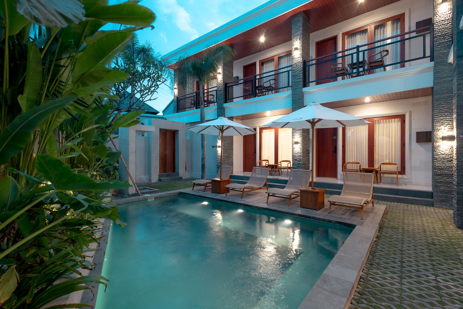 A poolside area with lounge chairs, umbrellas, and a two-story building with balconies.