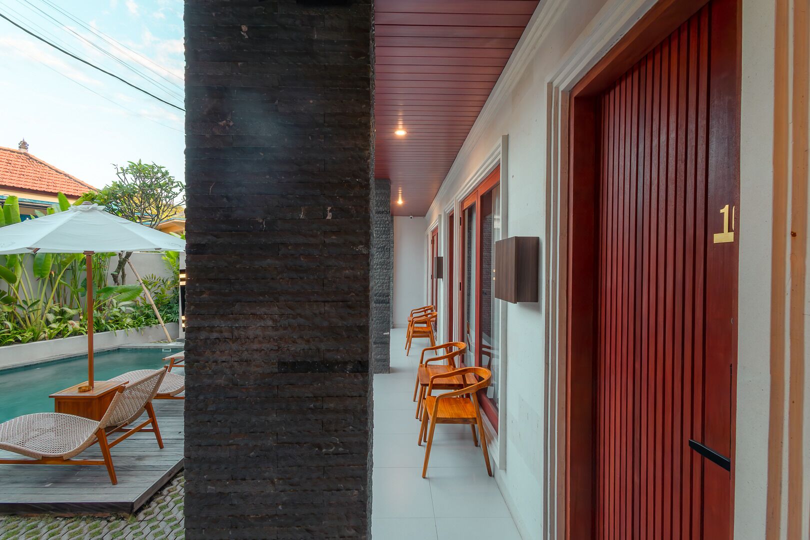 A poolside area with lounge chairs, a tiled floor, and a red door.