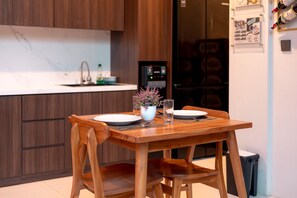 A wooden dining table with two chairs, a white plate, a glass, and a vase with flowers. - Casa Nika Suites Seminyak (Seminyak)