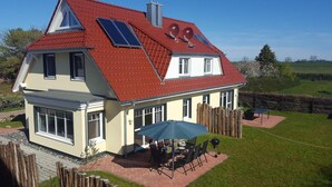 Una casa de dos pisos con techo rojo, paneles solares y un patio con mobiliario exterior.
