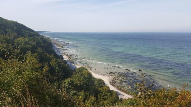 Un paisaje costero con una playa, costa rocosa y vegetación densa.