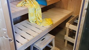 Una habitación de madera con literas, un pequeño taburete y un par de zapatos en el suelo.