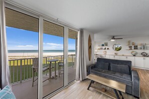 Un balcon avec vue sur la plage, un canapé gris et une table à manger.