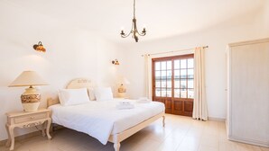 Een slaapkamer met een bed, nachtlampjes, een kroonluchter, een raam met gordijnen en een kledingkast.
