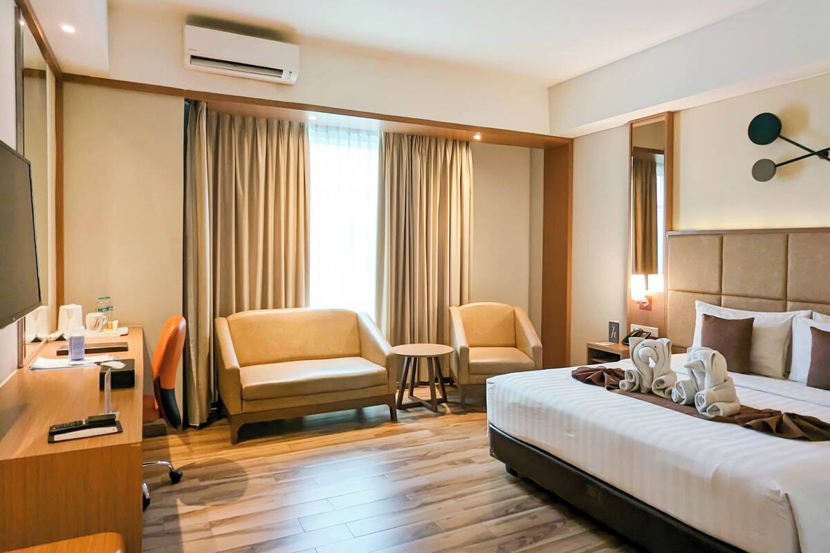 Een hotelkamer met een bed, twee banken, een bureau, een stoel, een bijzettafeltje en een airconditioning.