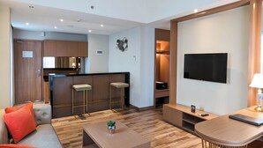 Een moderne woonkamer met een bank, salontafel en een televisie. Er is een keukenhoek met een bar en krukken.