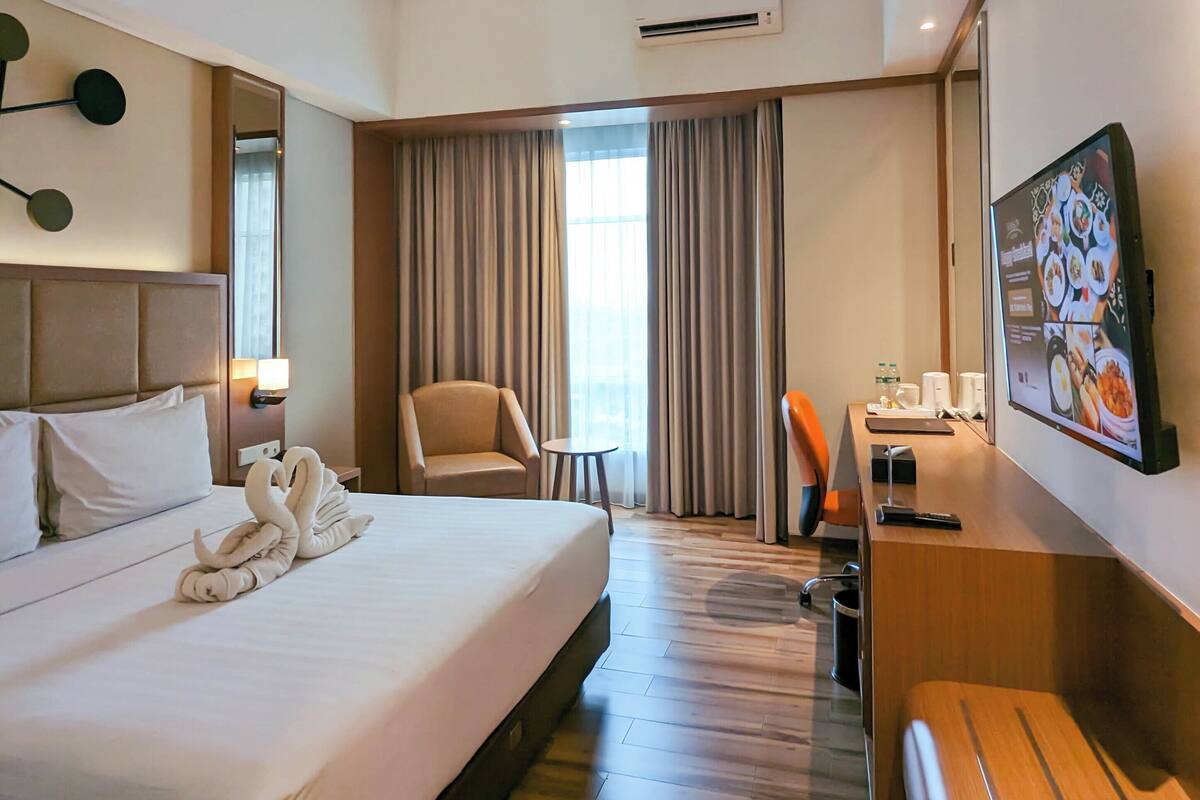Een hotelkamer met een groot bed, een bureau, een stoel, een televisie en een raam met gordijnen.
