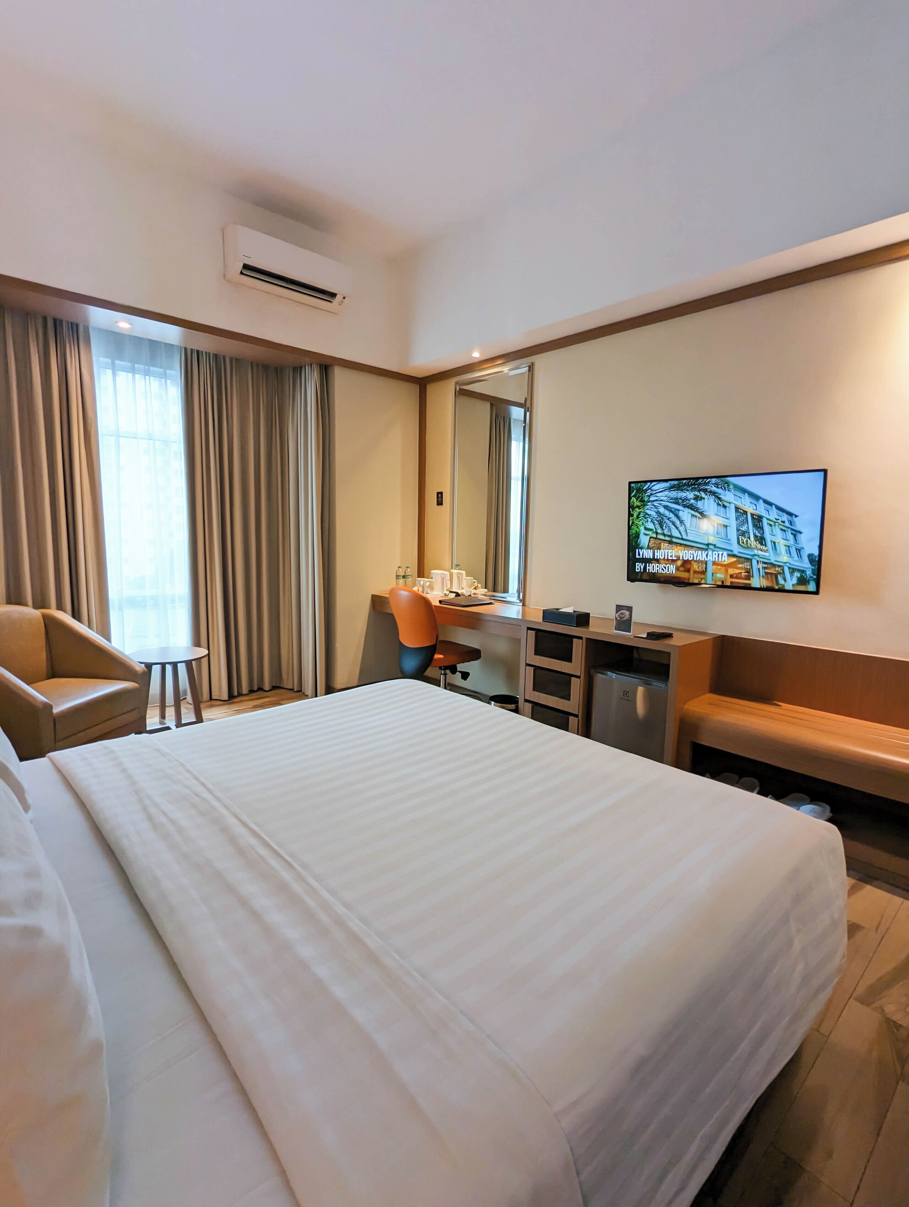 A hotel room with a large bed, a desk with a chair, a television, and a bathroom area.