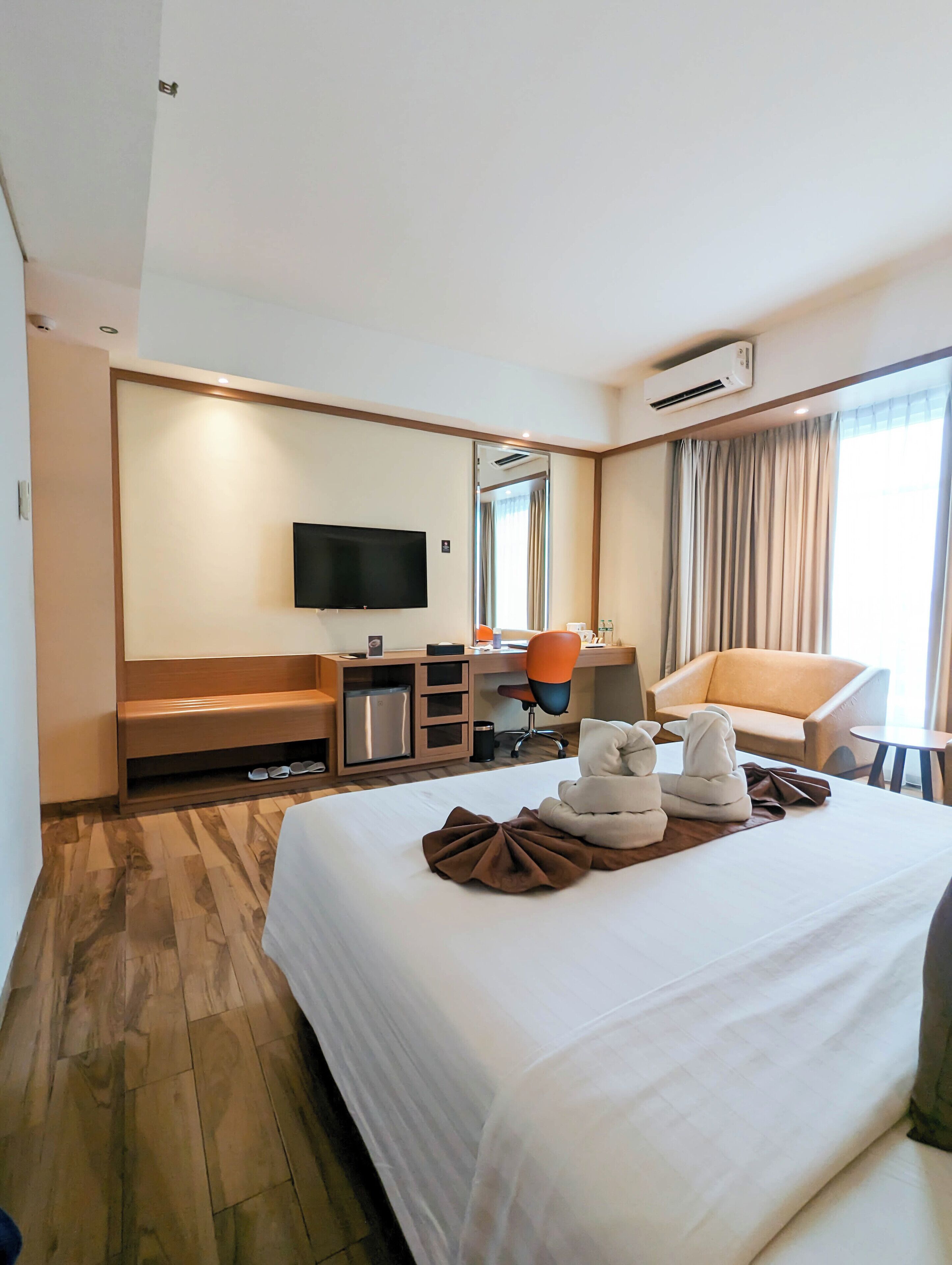 A hotel room with a large bed, a flat-screen TV, a desk with a chair, a sofa, and a small table.