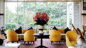 Een kamer met gele stoelen, een groot raam en een bloemenvaas.