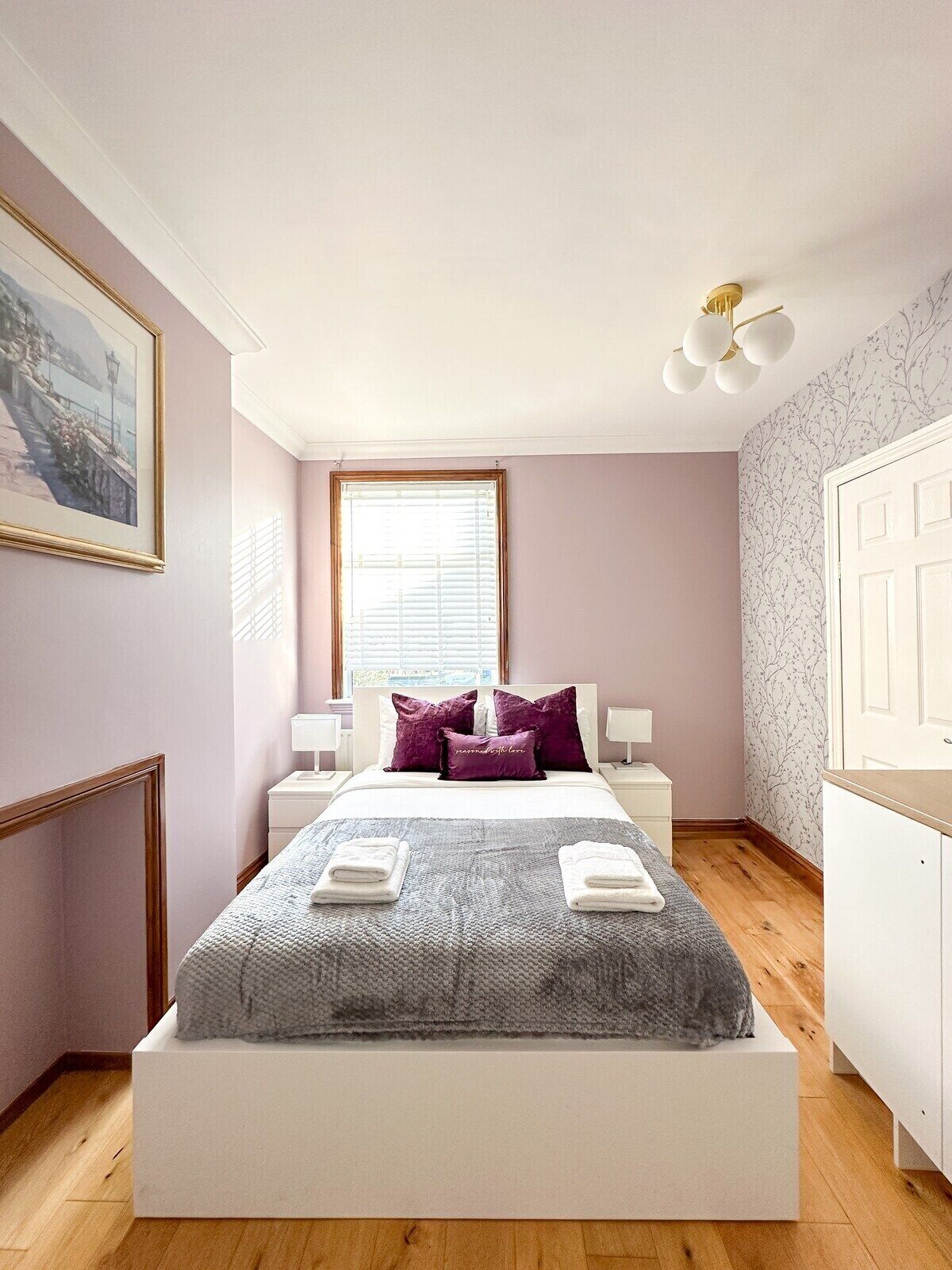 A bedroom with a bed, bedside tables, a window, a painting, and a wardrobe.