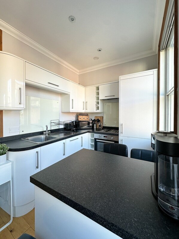 A modern kitchen with white cabinets, a black countertop, and a built-in stove. - Fulham Rooms (London)