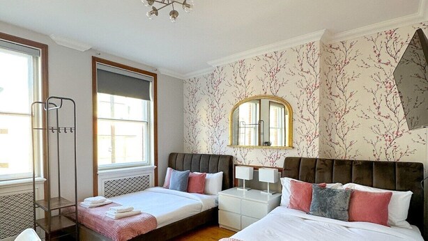 A hotel room with two beds, a large mirror, a radiator, and a window. - Fulham Rooms (London)